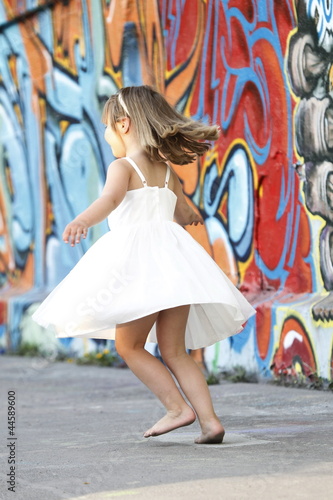 Kleines Mädchen in weißem Kleid tanzt vor Graffiti Wand