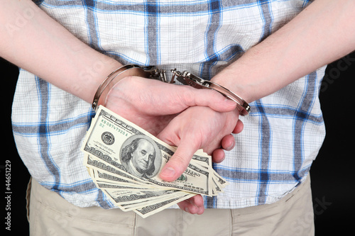 man in handcuffs is holding dollars, on black background photo