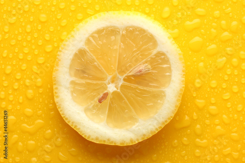 Slice of lemon with drop on yellow background