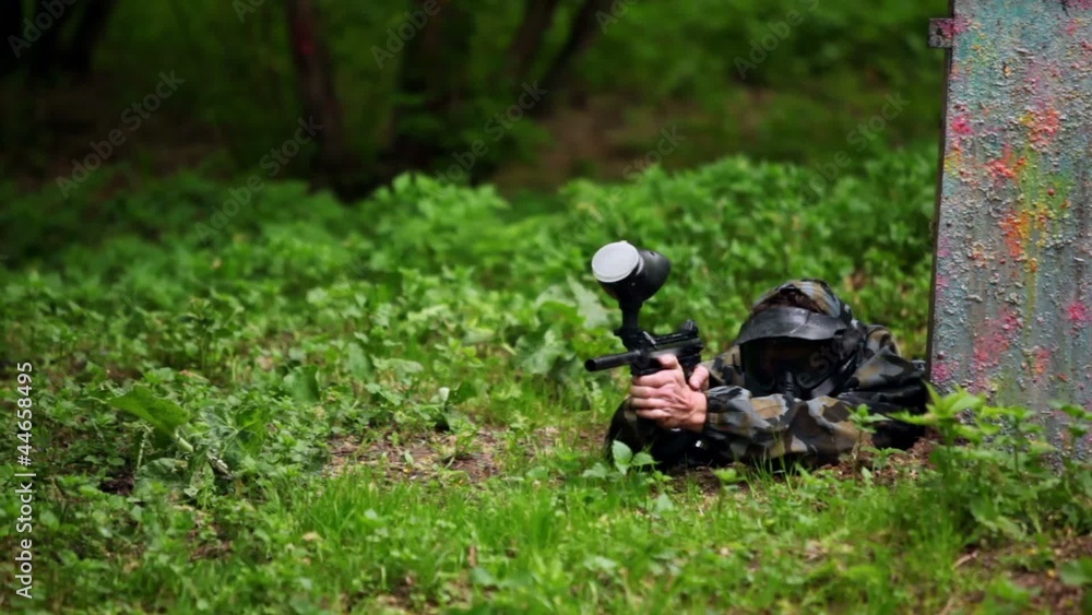 Boy paintball player lies with gun in ambush on grass Boy paintball player lies with gun in ambush on grass