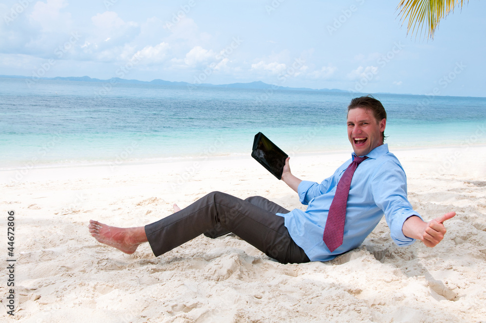 Happy business man sitting and working on the beach with tablet