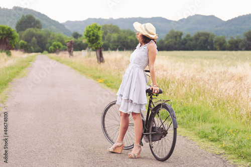 Pretty young woman relaxing with bike in a country road.