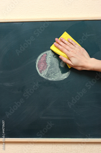hand with a yellow sponge cleaning the chalkboard © Africa Studio