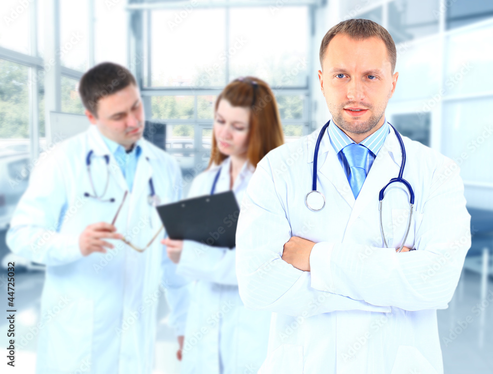 Portrait doctor smiling with colleagues in background Portrait doctor smiling with colleagues in background