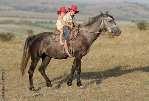 two young happy children riding horse
