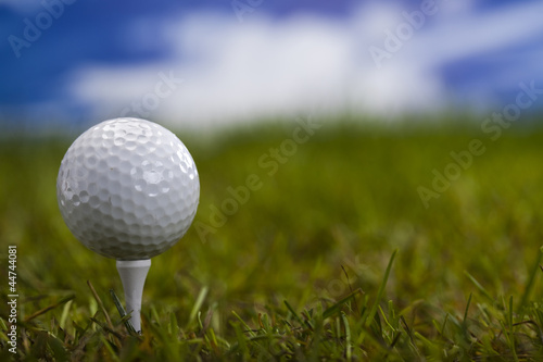 Golf ball on green grass over a blue sky 
