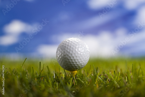 Golf ball on green grass over a blue sky 