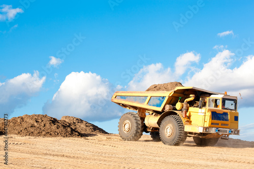 Heavy dump truck unloads soil on the sand at a construction site