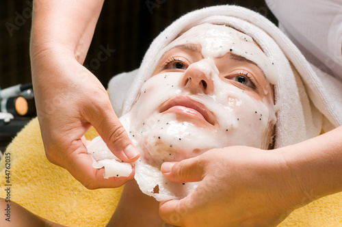 Cosmetician taking facial mask off the face of a young woman
