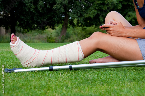 Girl with leg in plaster chatting with her smartphone