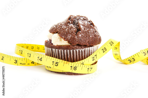 Chocolate muffin with a tape measure around it on white