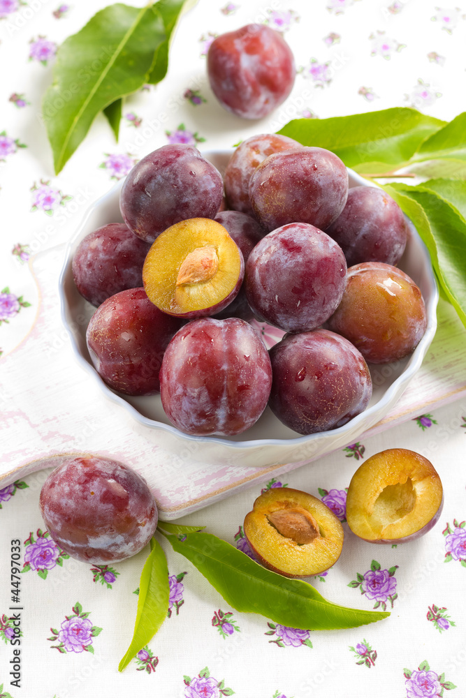 Fresh wet plums with leaves in the bowl on the vintage board Fresh wet plums with leaves in the bowl on the vintage board