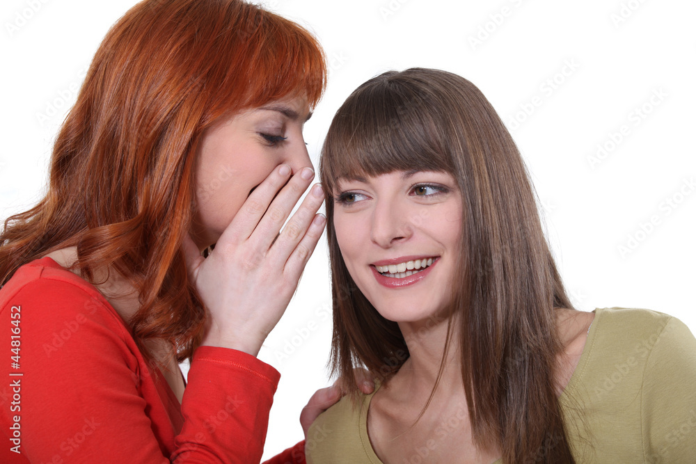 Young woman whispering a secret into her friend's ear Young woman whispering a secret into her friend's ear