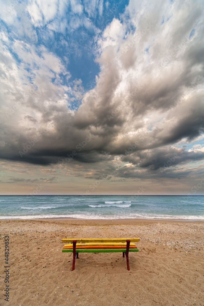 colorful bench on a beach dramatic clouds and sea as backdrop