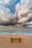 colorful bench on a beach dramatic clouds and sea as backdrop