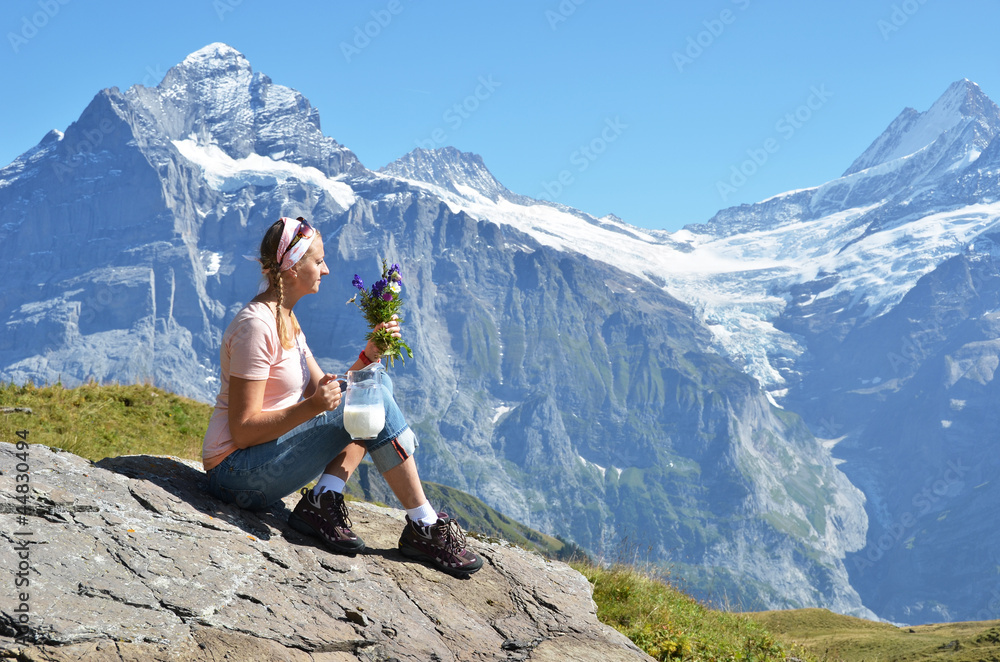 Girl with a jug of milk and flowers against Swiss Alps