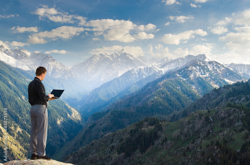 Young businessman using his laptop on the mountain top