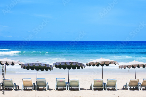 Beach chairs on the white sand beach with cloudy blue sky © butter45