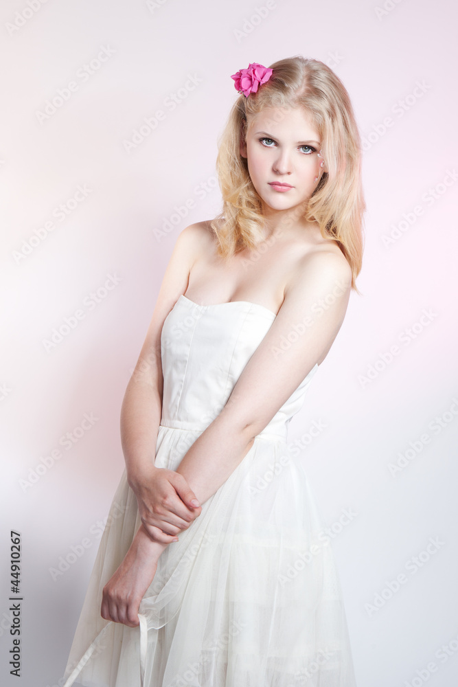 Young blonde girl posing in studio in white dress