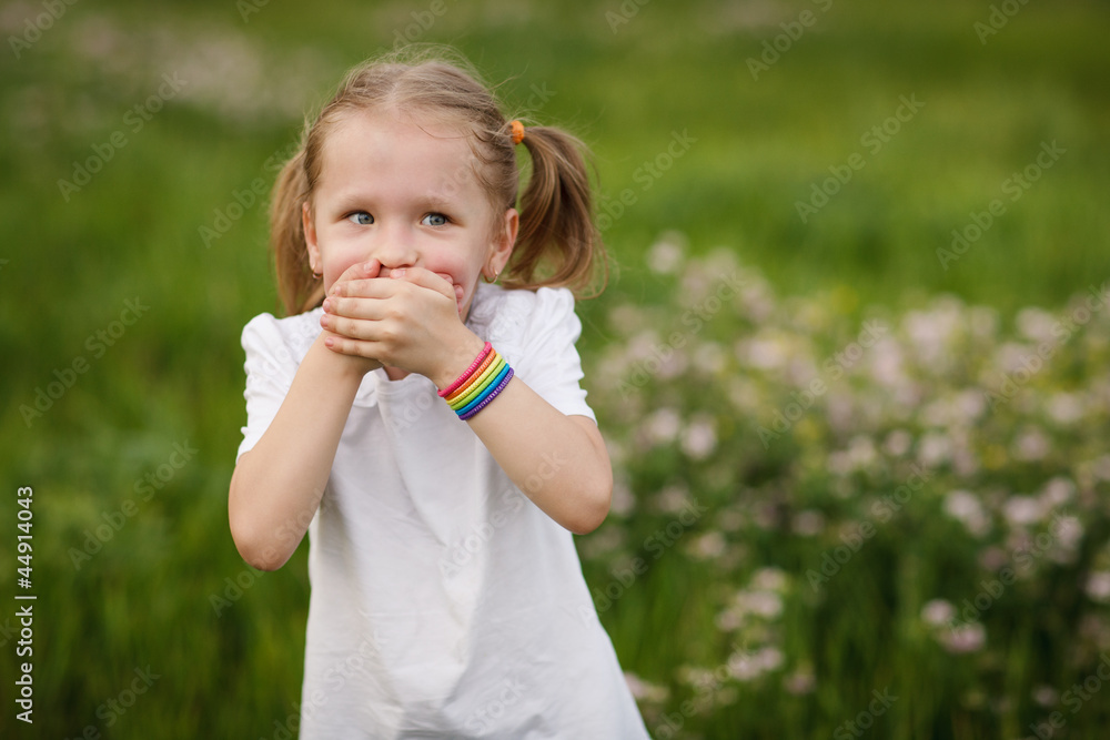 Playful little girl covering her mouth with palms outdoors Playful little girl covering her mouth with palms outdoors