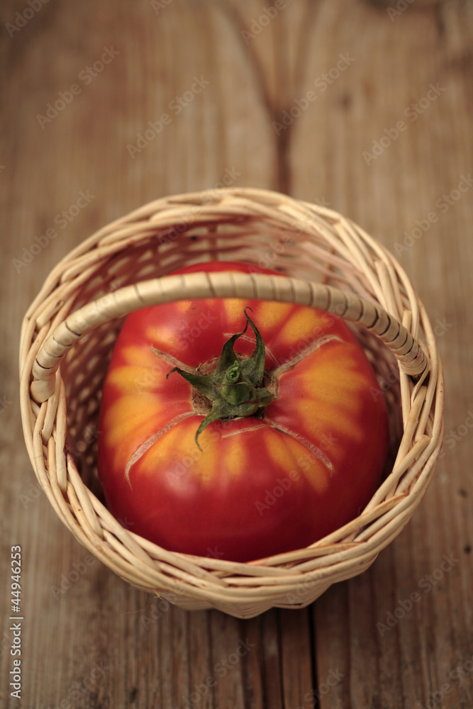One big ripe tomato in a basket on wooden background