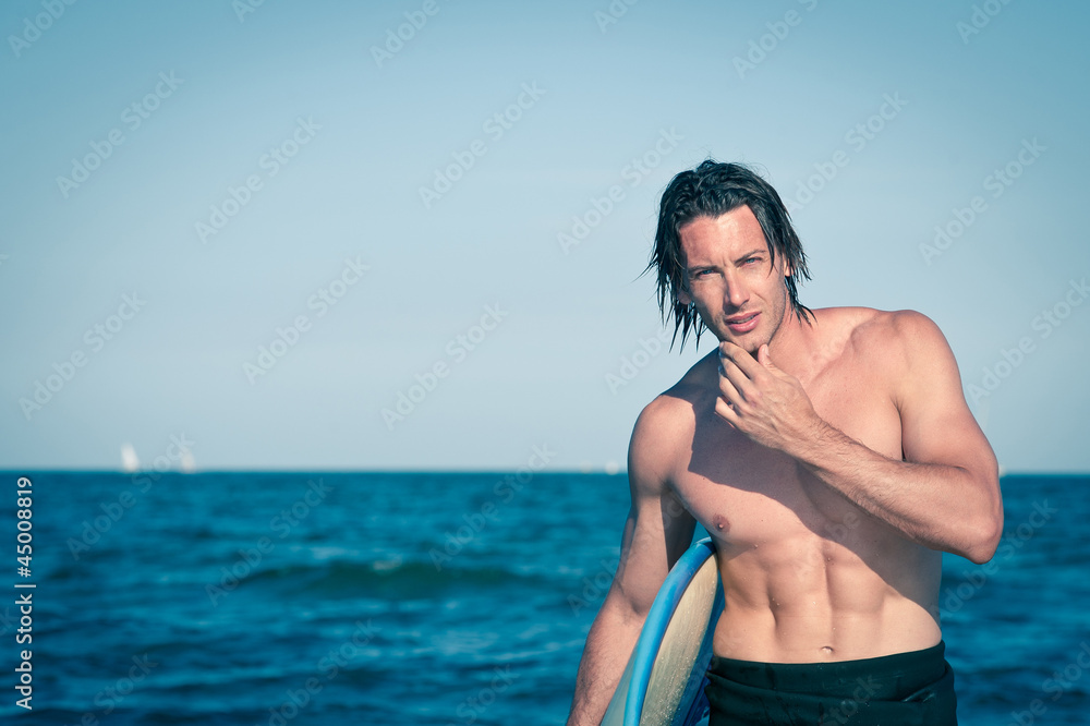 Attractive young surfer portrait at the beach with a surfboard.