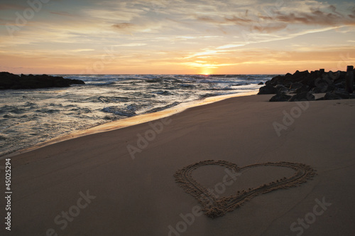 heart drawn in the sand on the beach at sunset