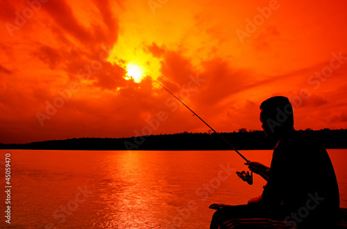 Silhouette of man fishing during sunset