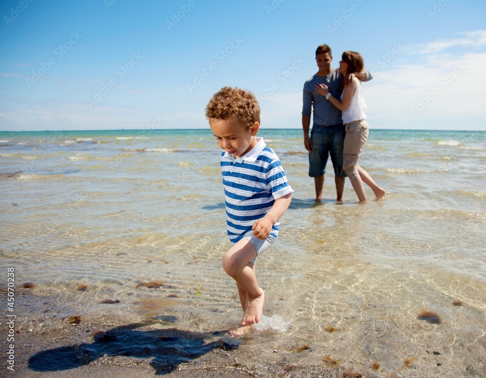 Young Couple Watches as Son Walks Away from the Water Young Couple Watches as Son Walks Away from the Water
