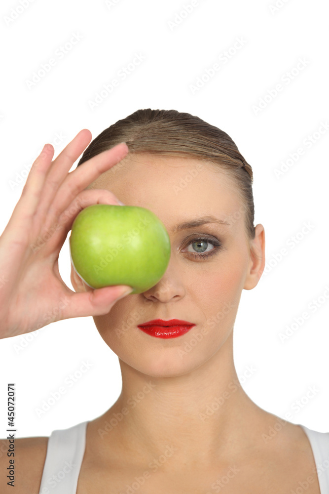 Woman holding green apple over her eye Woman holding green apple over her eye