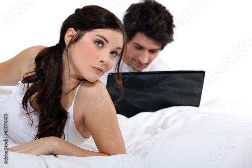 Man with laptop and woman in bed