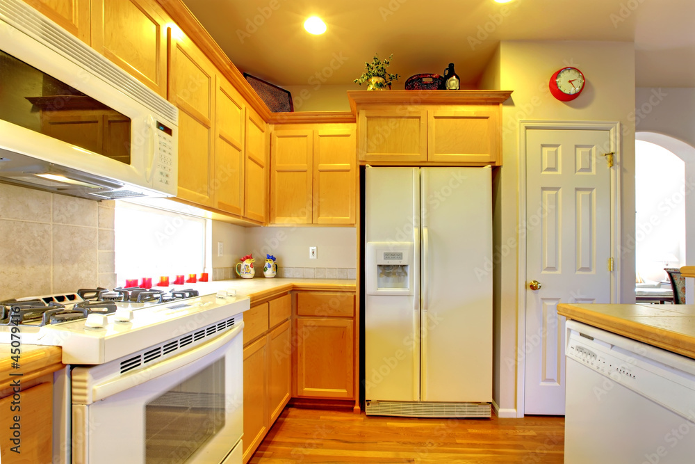 Fototapeta premium Kitchen with yellow wood cabinets and white appliances.