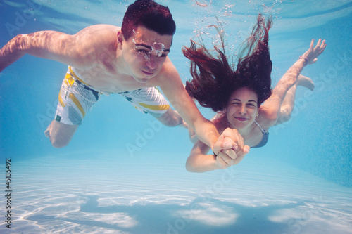 Underwater couple holding hands in swimming pool. 