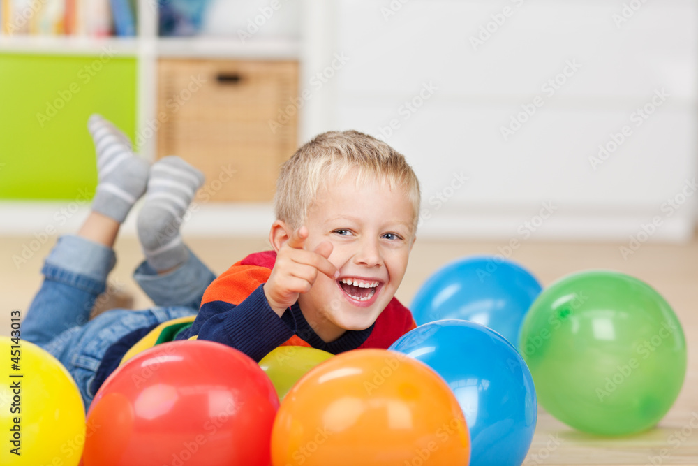 Obraz premium kleiner junge liegt zwischen bunten luftballons