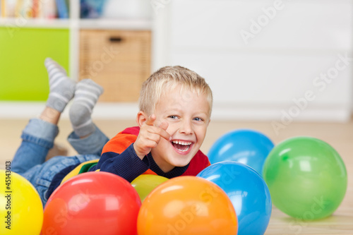 kleiner junge liegt zwischen bunten luftballons
