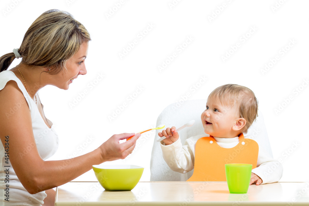 young mother spoon feeding her cute baby girl isolated on white young mother spoon feeding her cute baby girl isolated on white