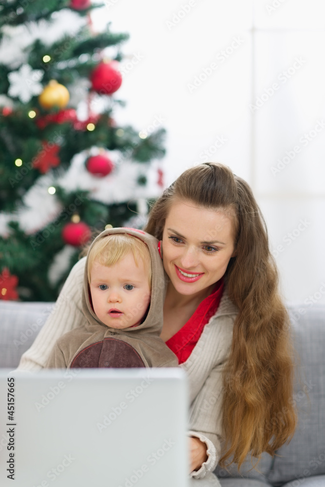 Mother and baby near Christmas tree using laptop Mother and baby near Christmas tree using laptop