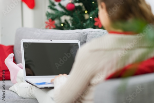 Woman using laptop near Christmas tree. Rear view photo