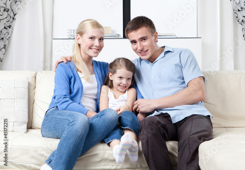 Family of three hug each other on the white leather sofa