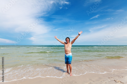 Мужчина стоит на пляже, радостно раскинув руки в стороны.