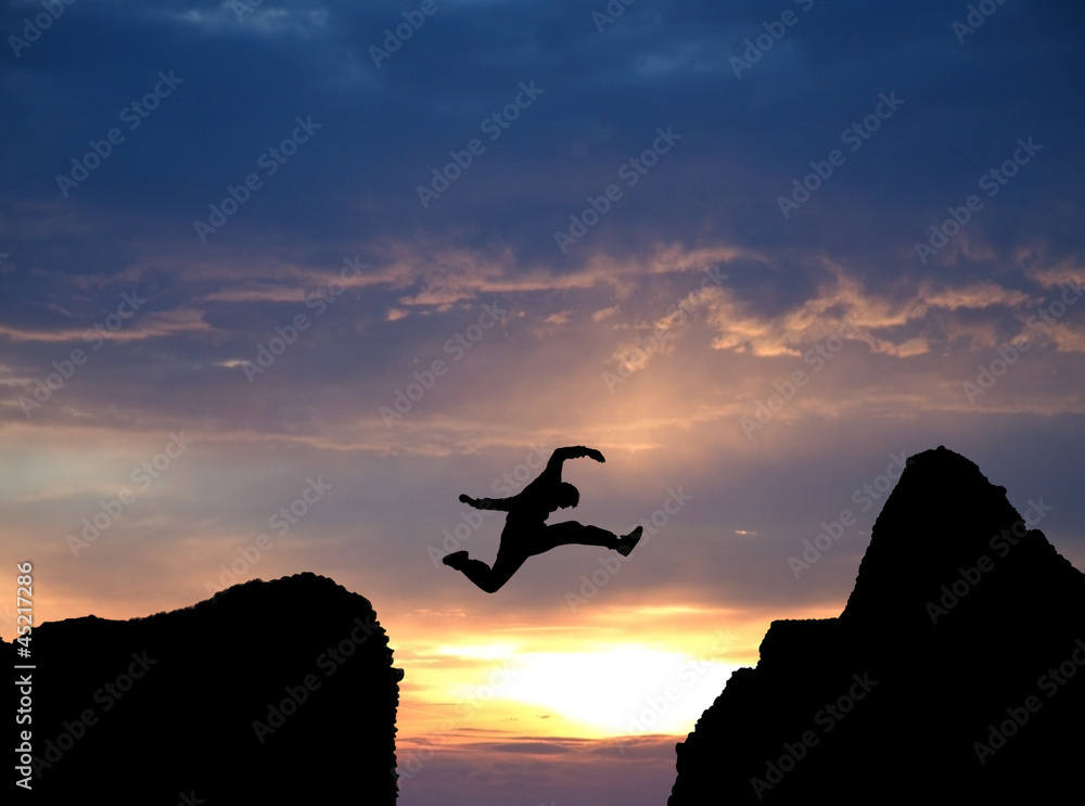 silhouette of man jumping over rocks in sunset