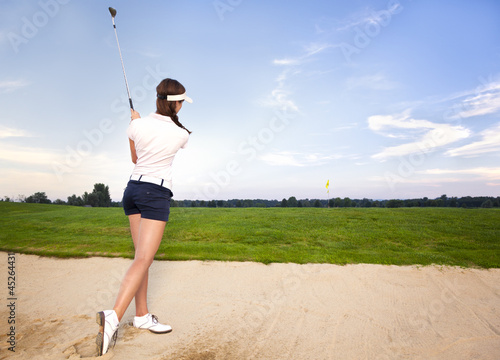 Girl golf player in bunker chipping ball.