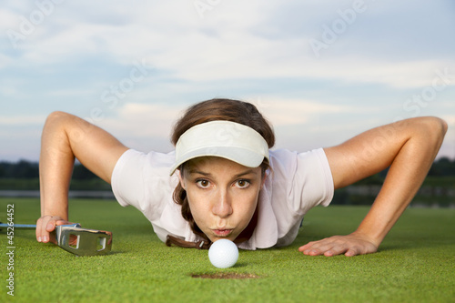 Girl golf player blowing ball into cup.