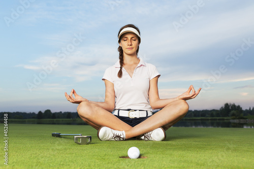 Girl golfer sitting in yoga posture on golf course.