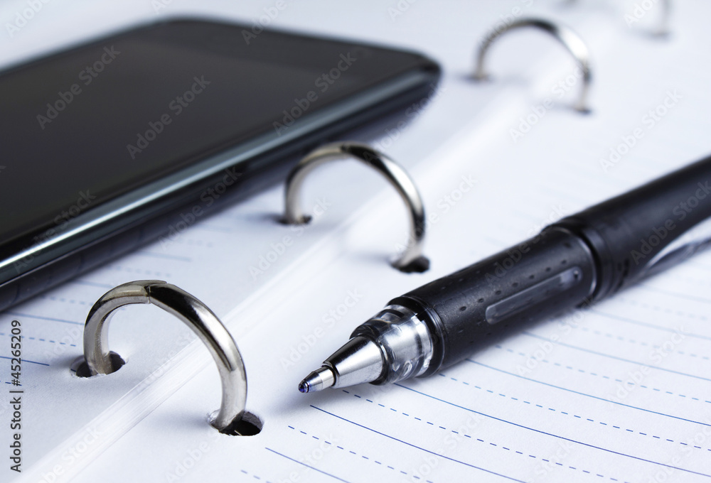 closeup of pen, spiral notebook and cell phone closeup of pen, spiral notebook and cell phone