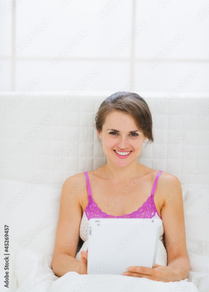 Happy young woman sitting on bed with tablet PC Happy young woman sitting on bed with tablet PC