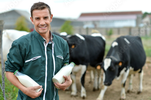 Fotografia Farmer standing in front of cow herd with bottles of milk