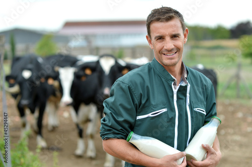 Принти на полотні Farmer standing in front of cow herd with bottles of milk