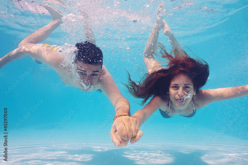 Underwater couple holding hands in swimming pool.