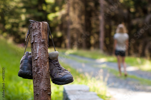 Abandoned hiking shoes with a woman walking bare fee